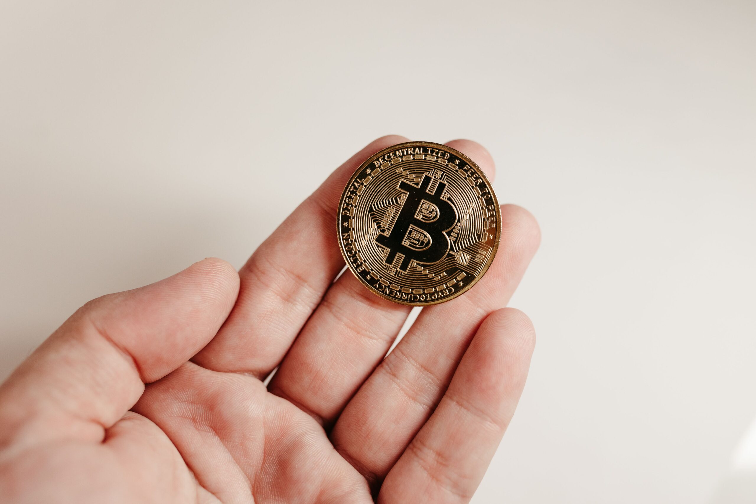 A close-up image of a Bitcoin coin held in a human hand against a white background.